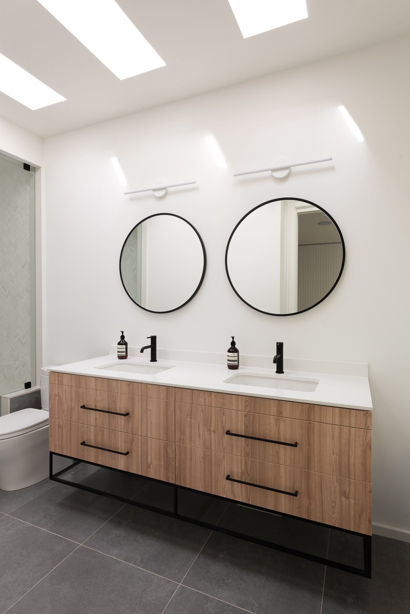 Double vanity with oak drawers, twin round mirrors, and white countertop.