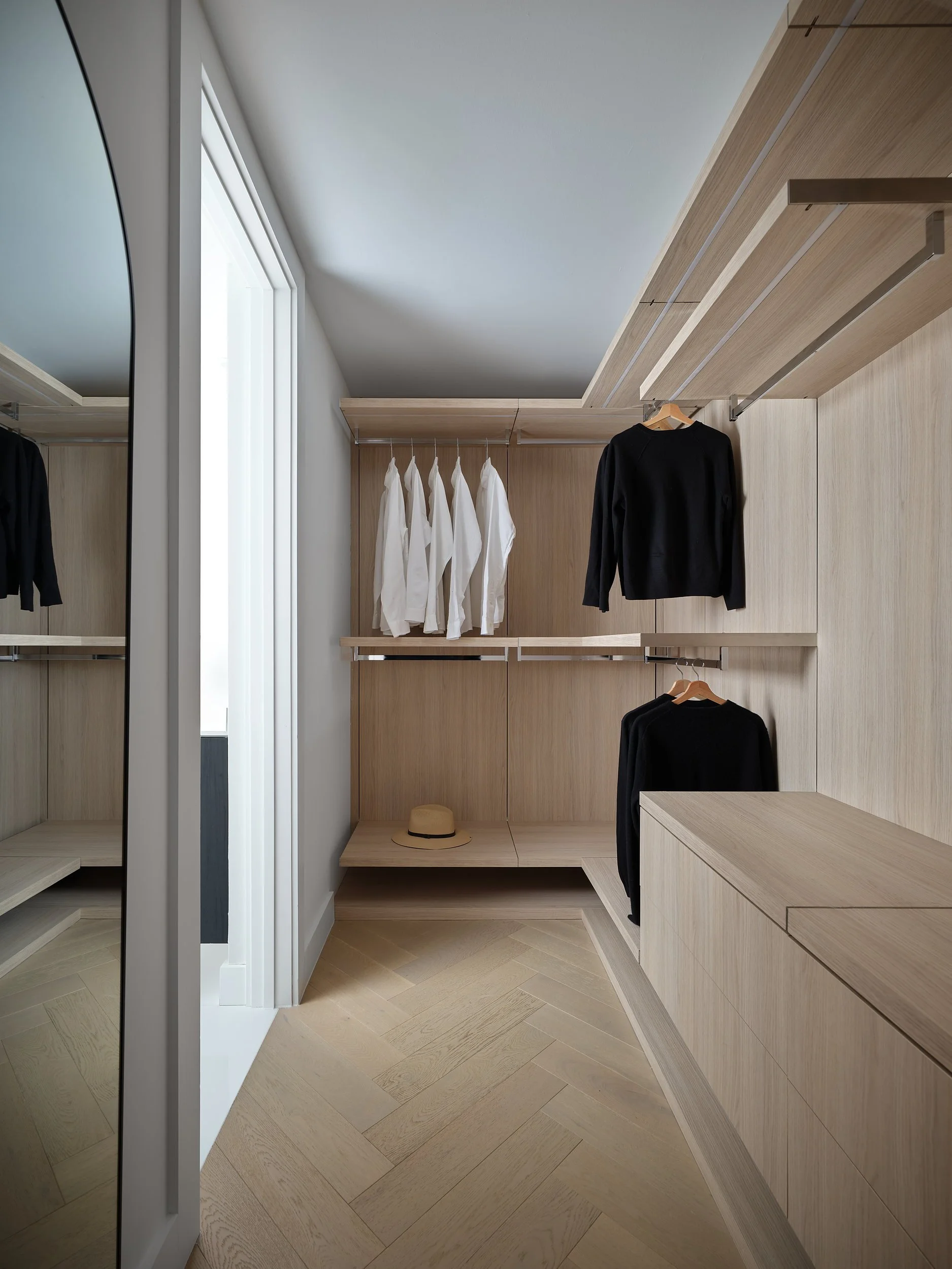 Walk-in wardrobe with oak shelving, hanging rails, and low drawer bench.