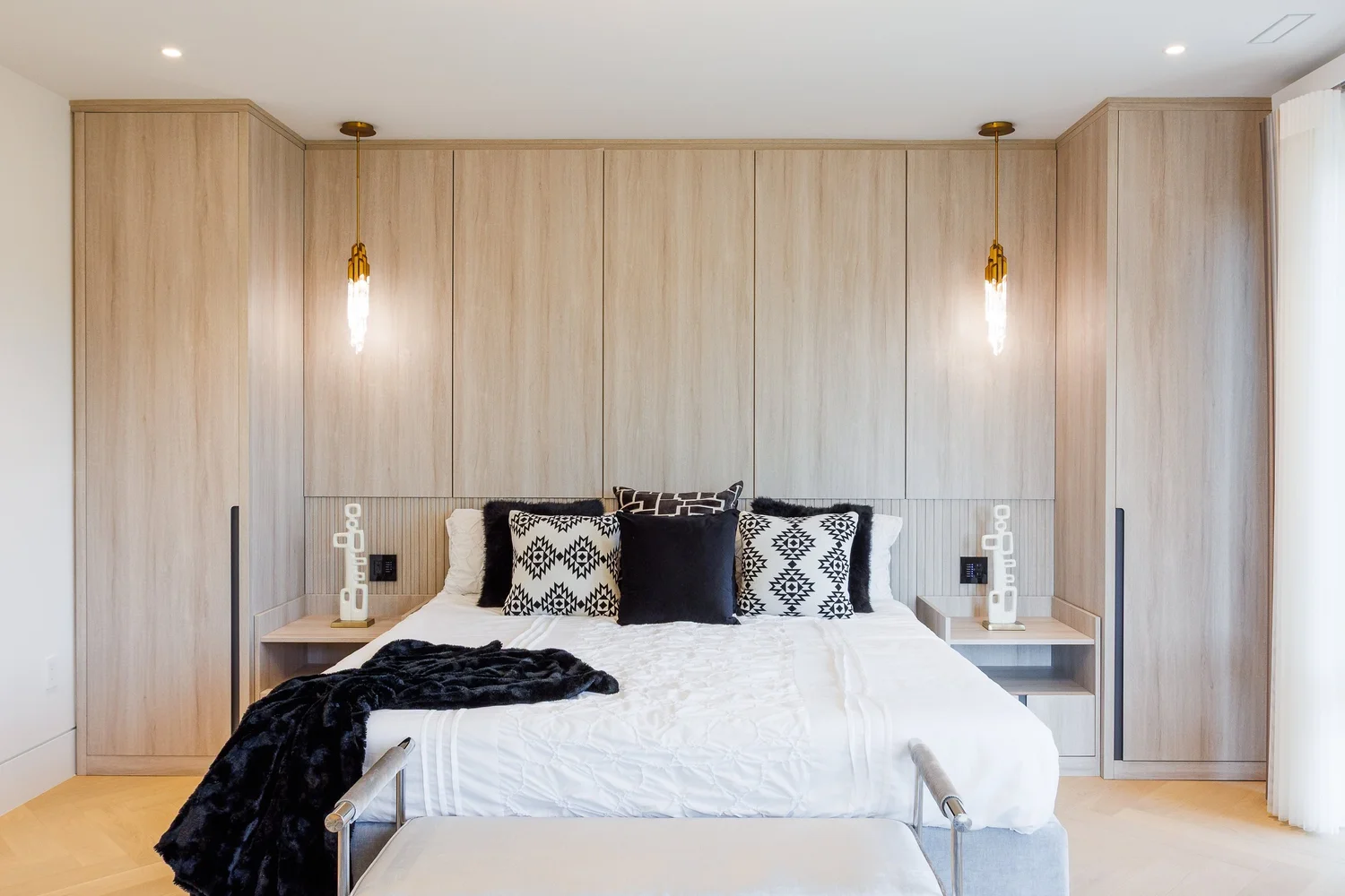 Primary bedroom with a full-width wardrobe wall, integrated headboard, and pendant lights.