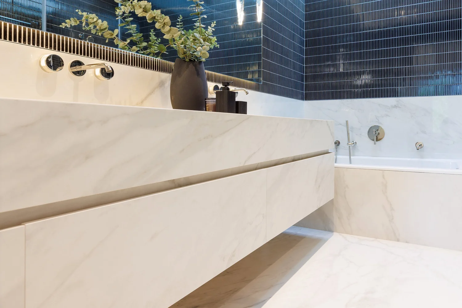 Ensuite with a long floating stone vanity running toward the tub, against dark tile.