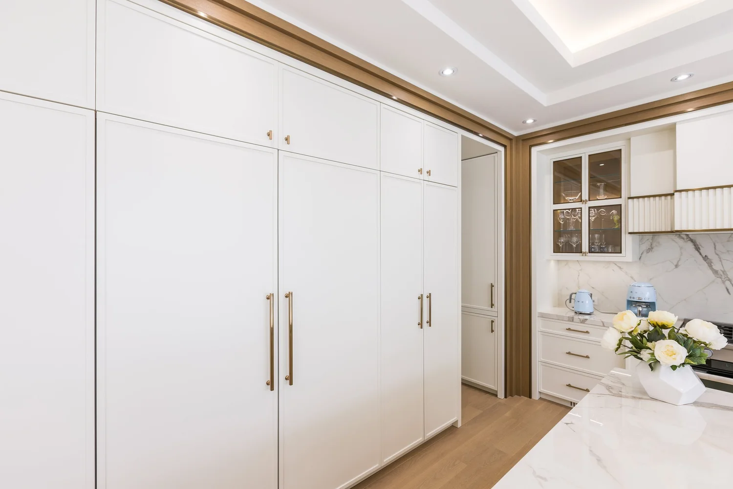Full-height white cabinet wall framed in oak, beside the marble island.