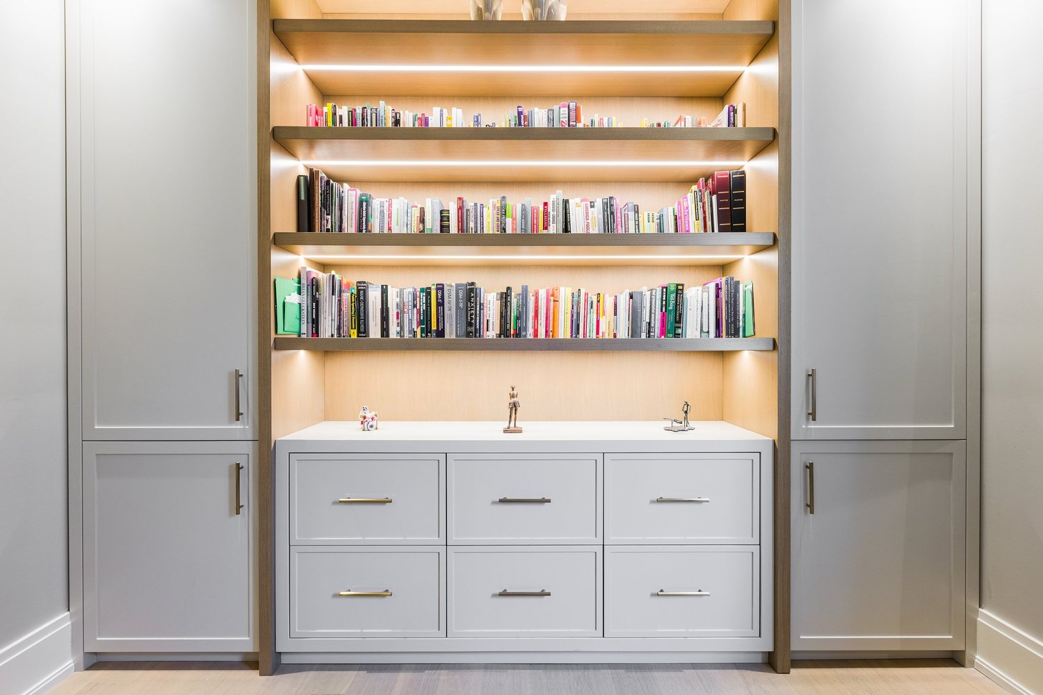 Study with illuminated library shelving above a grey drawer unit.