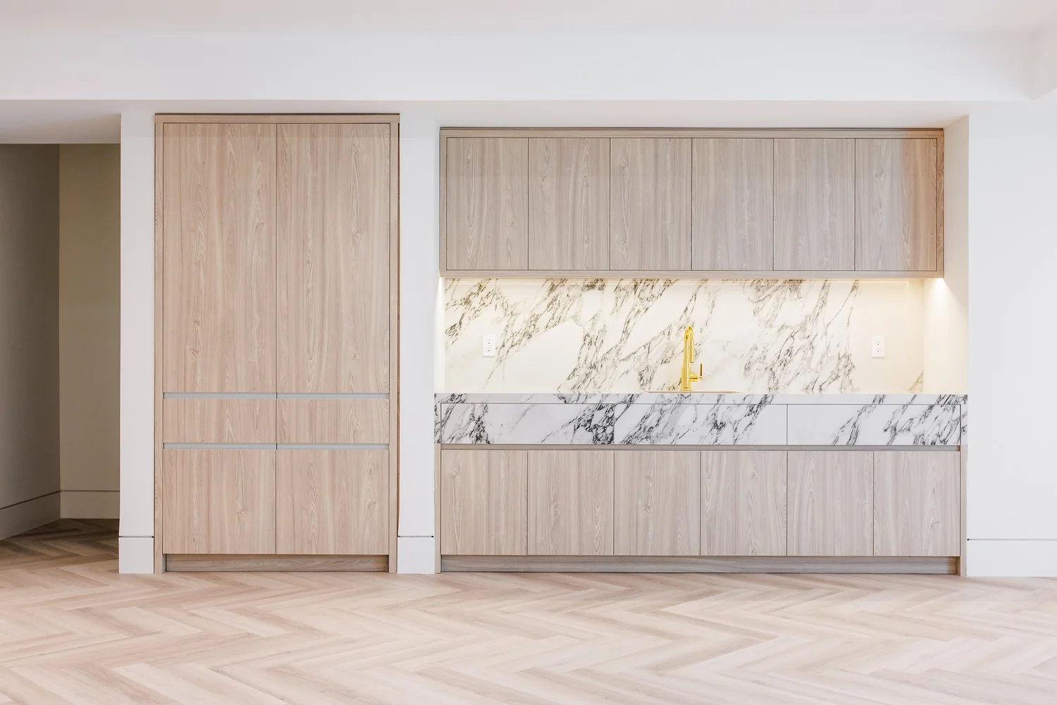 Lower-level kitchenette in light oak with a marble backsplash and brass tap.