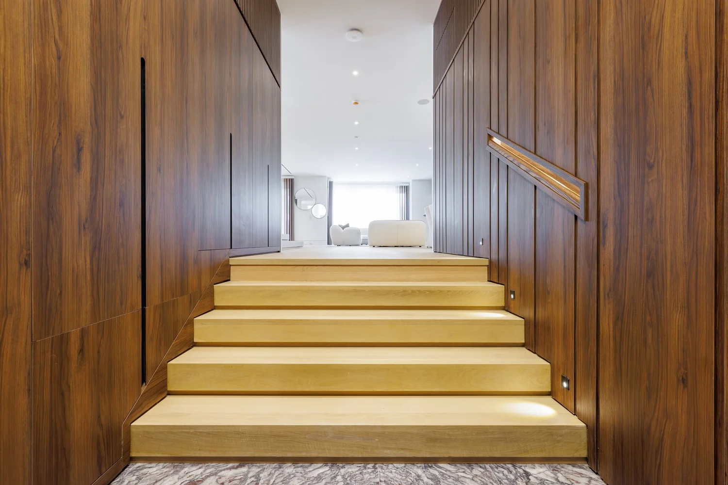 Oak stair treads rising between walnut-panelled walls with an integrated handrail.