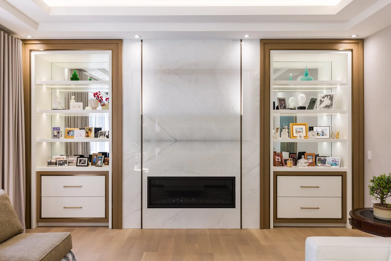 Family room feature wall in white marble with brass inlays, a linear fireplace, and illuminated display niches.