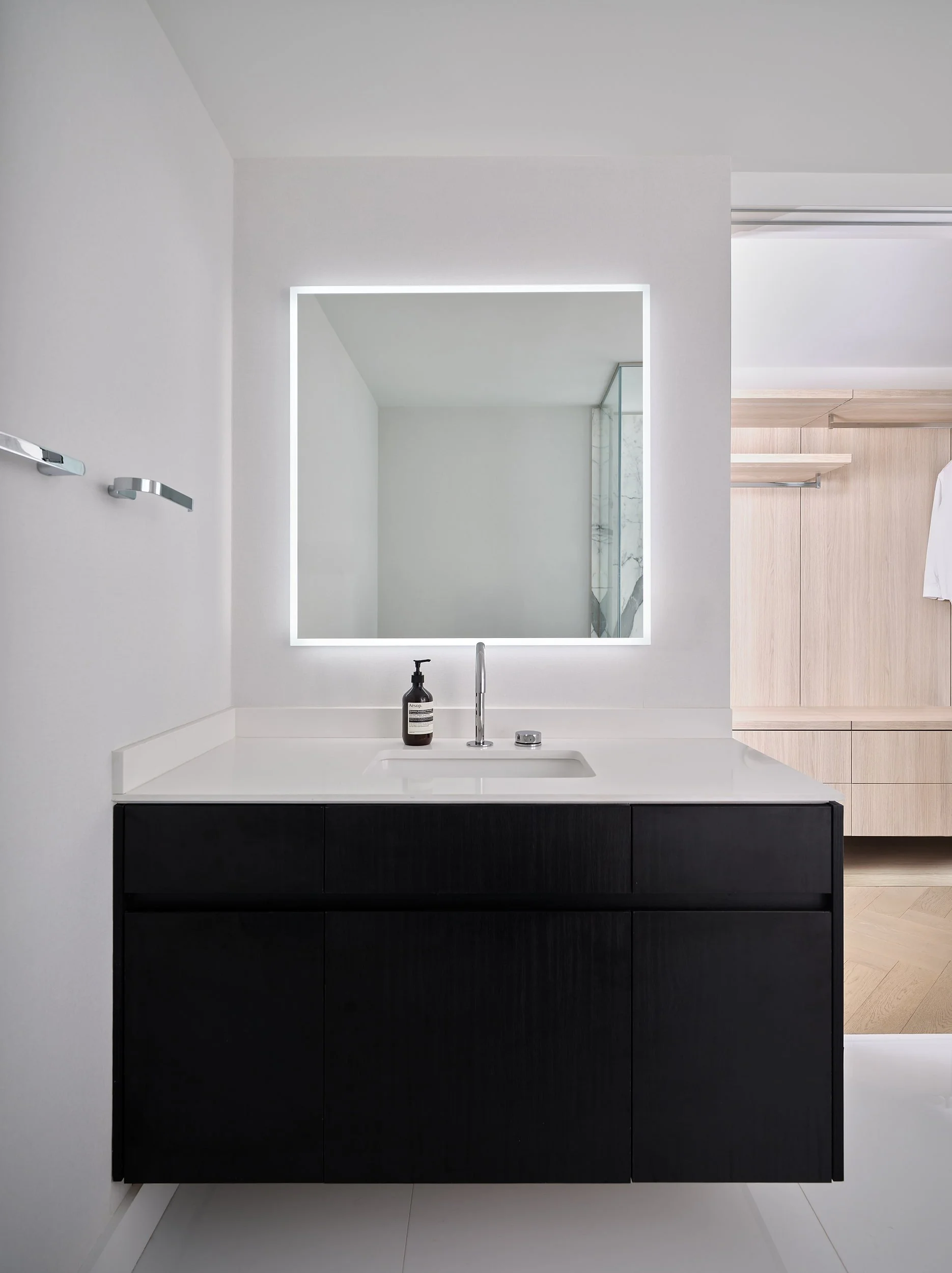 Bathroom with floating dark oak vanity and backlit mirror, wardrobe beyond.