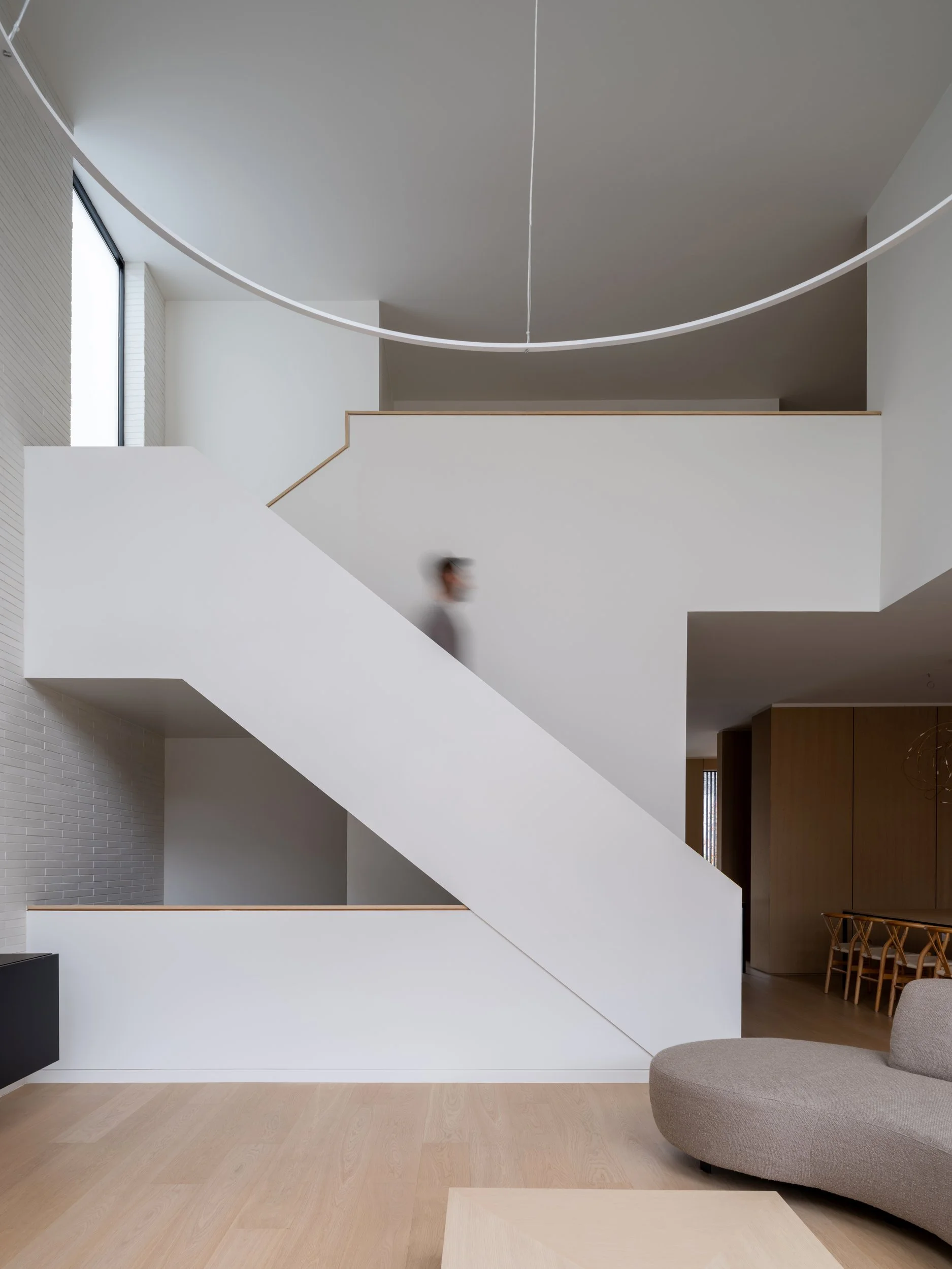 Sculptural white staircase with oak treads in a double-height space.