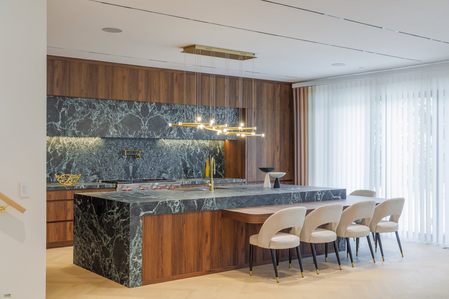 Kitchen island and dining table beside the window wall, with the marble cooking wall beyond.