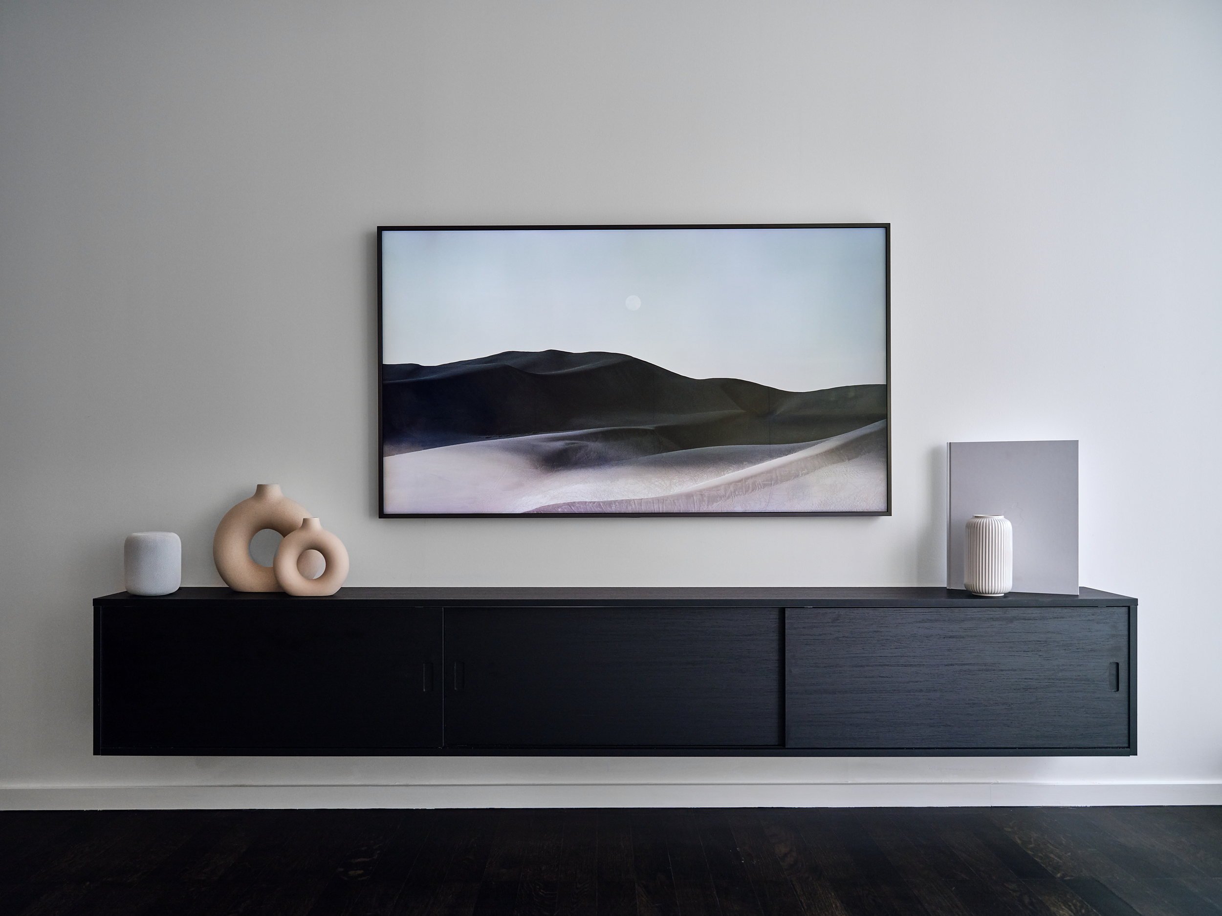 Wall-mounted black media console below a framed television.