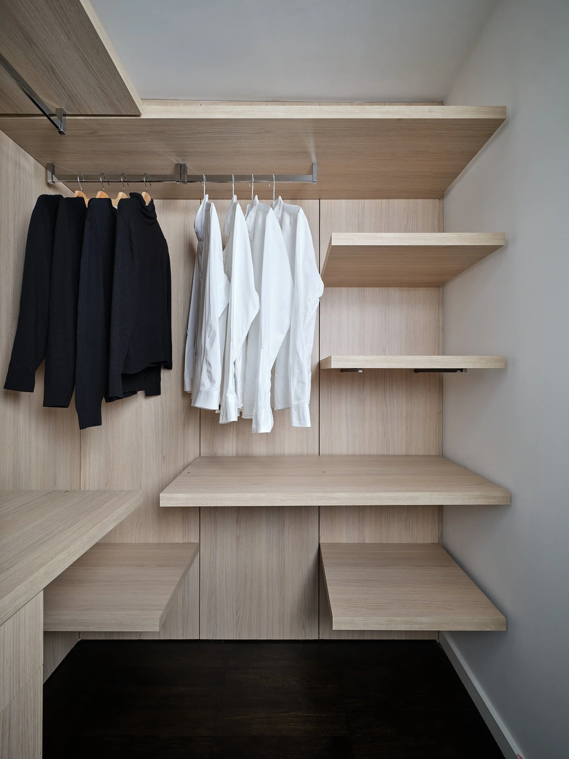 Walk-in closet with white oak shelving, drawers, and hanging rail.