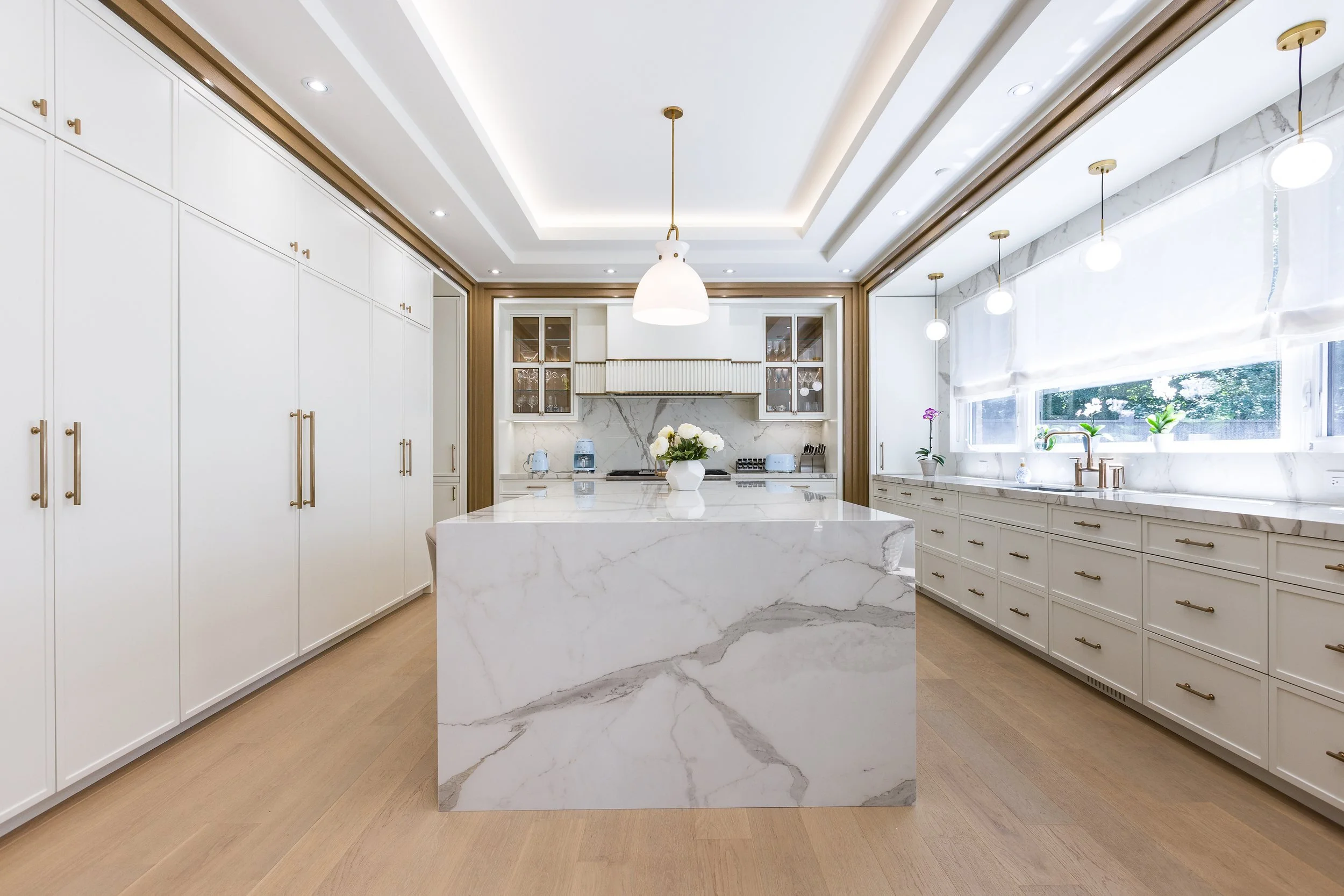 Michigan Drive Residence kitchen with a waterfall marble island, full-height white cabinetry, and oak trim.