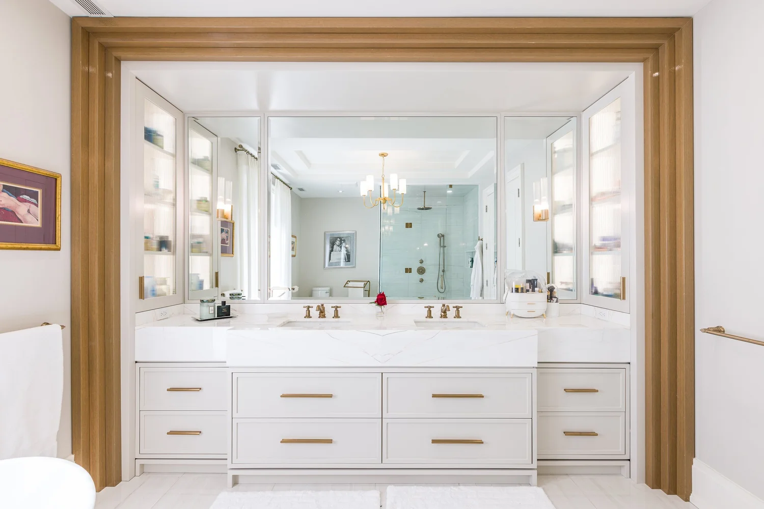 Primary ensuite double vanity framed in oak, with brass pulls and backlit mirrored cabinets.