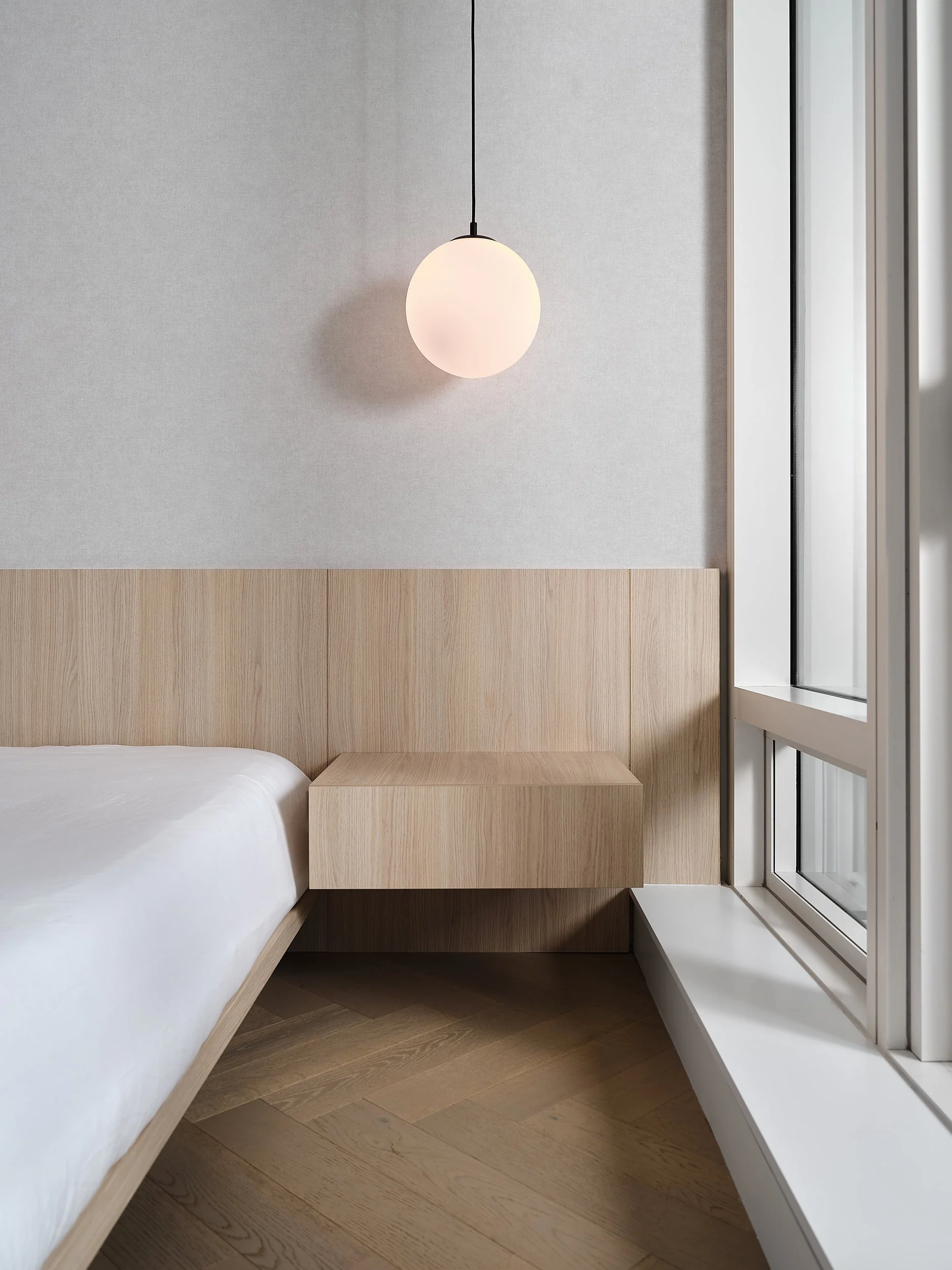 Bedroom with oak headboard panel, floating nightstand, and pendant light.
