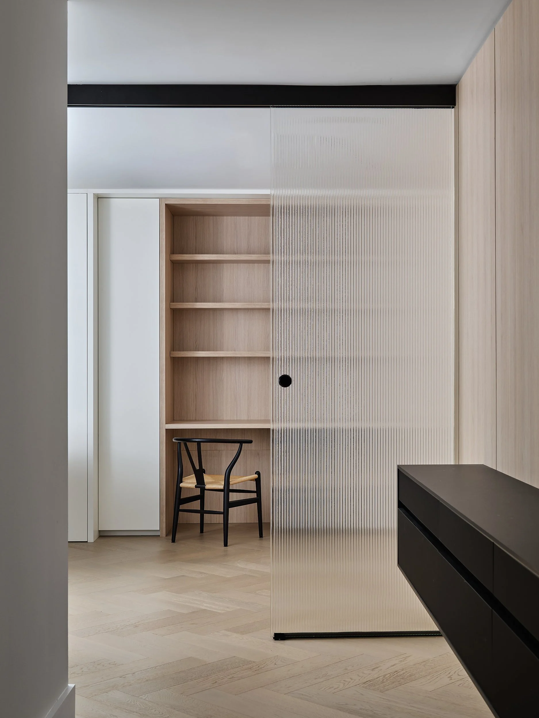 Den workspace with reeded glass partition, oak shelving, and floating black console.