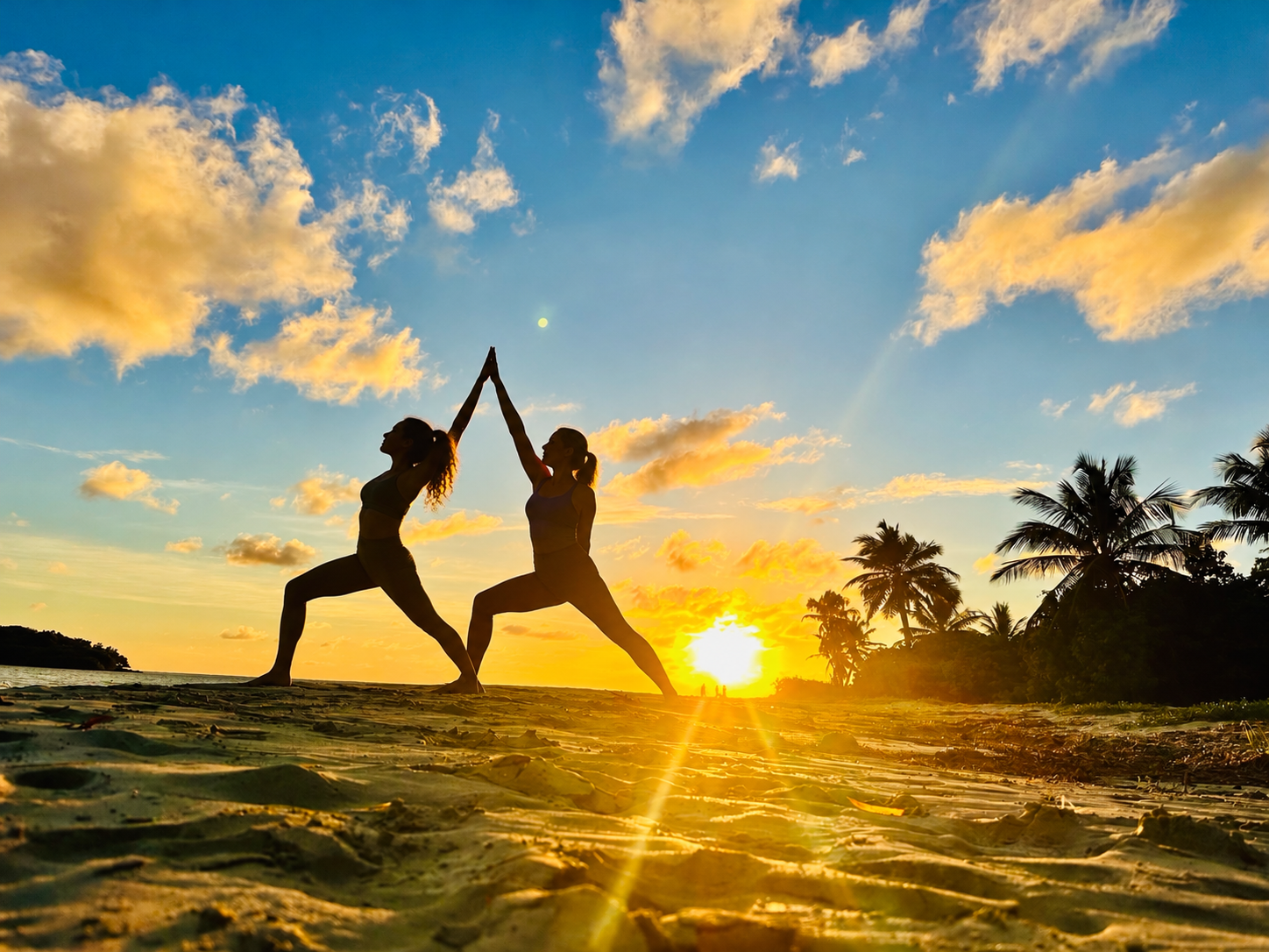 Two women sharing a partner yoga pose on the beach at sunset