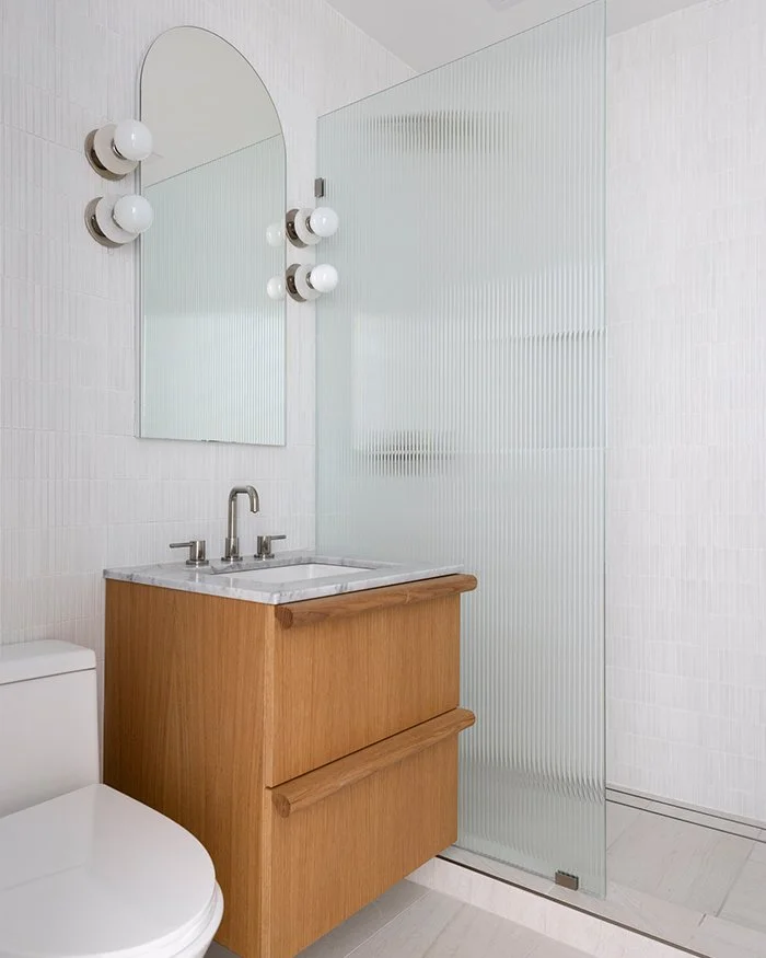 Modern white bathroom, floating wood vanity, fluted glass shower