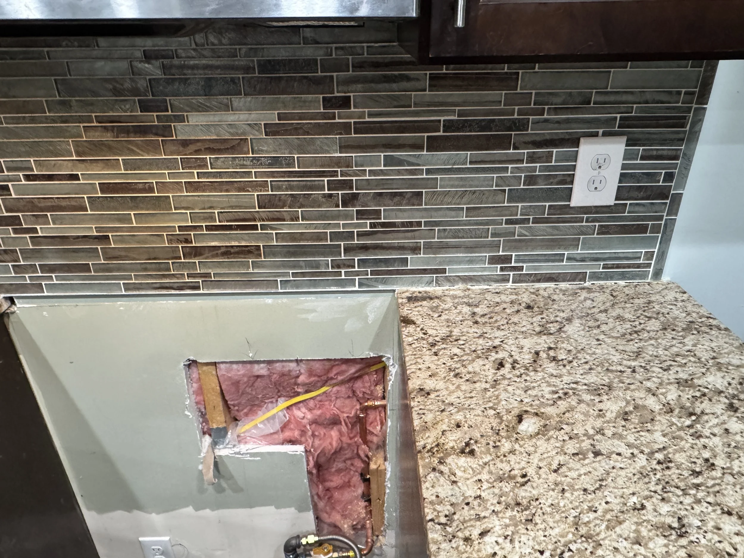 Wall opened below a kitchen receptacle so a new circuit can be run behind the finish