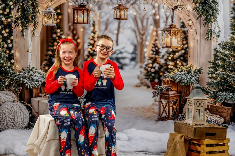 Siblings in matching Christmas pajamas holding mugs