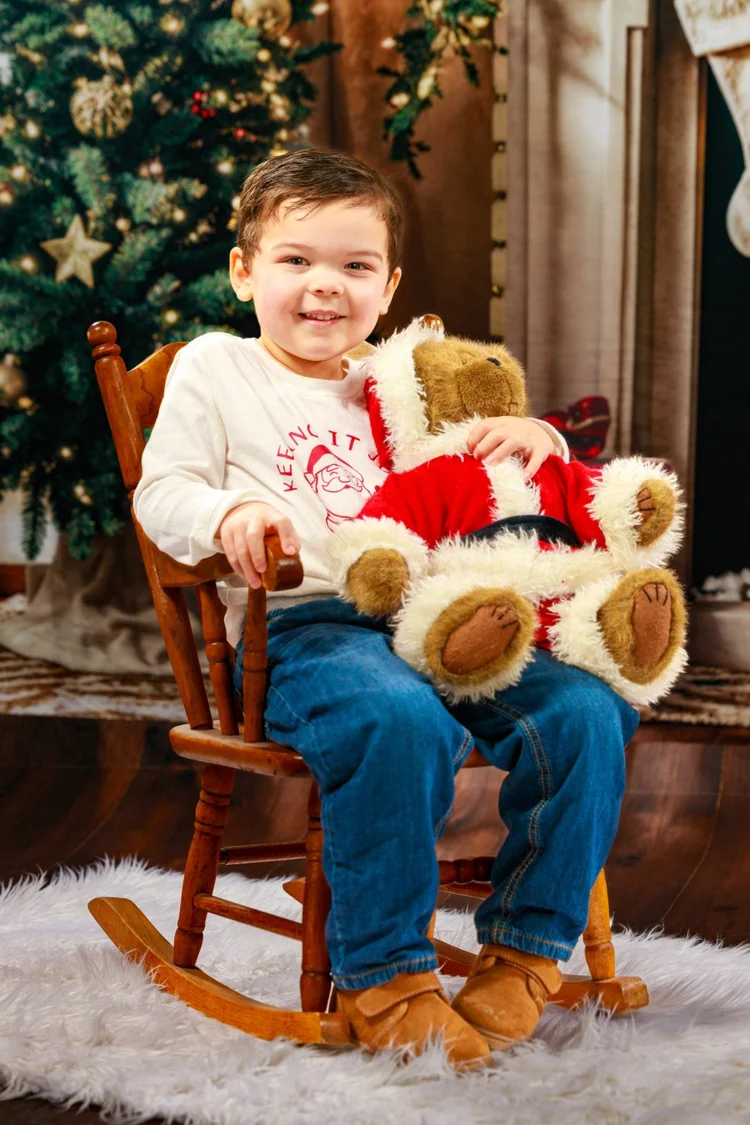 Young child holding a teddy bear in a Christmas studio set