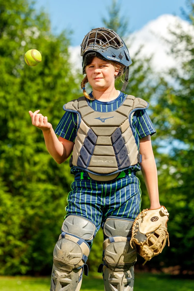 Youth softball catcher tossing a ball in uniform