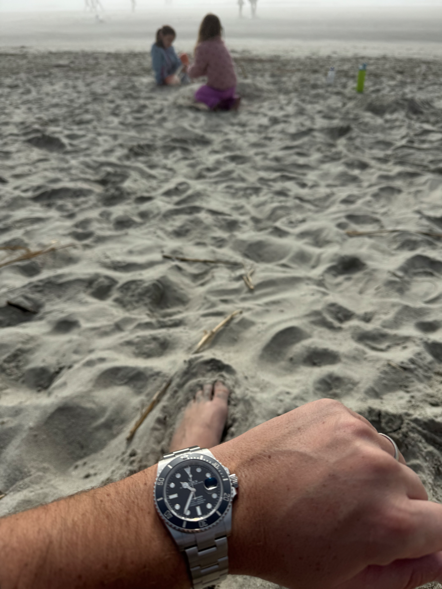 A watch on Jacob’s wrist with his daughters playing on the beach