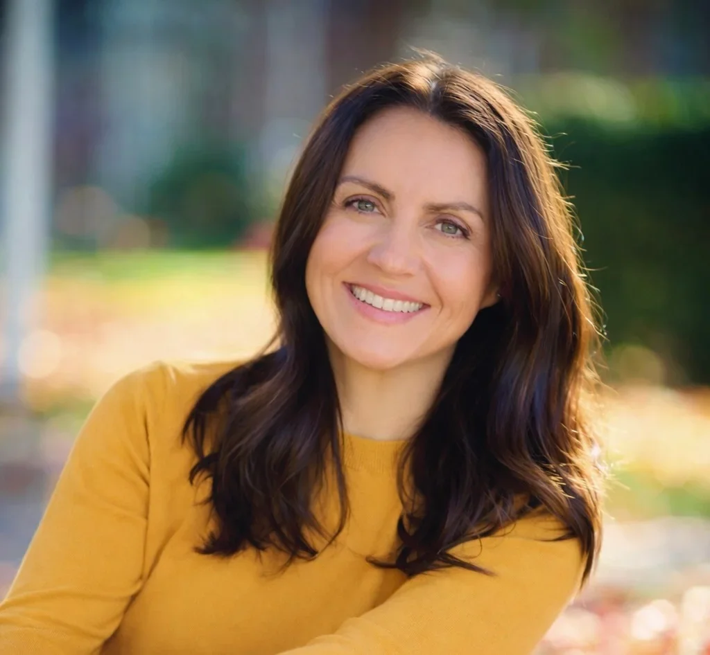 Genna Marie outdoors in a mustard sweater, smiling at the camera