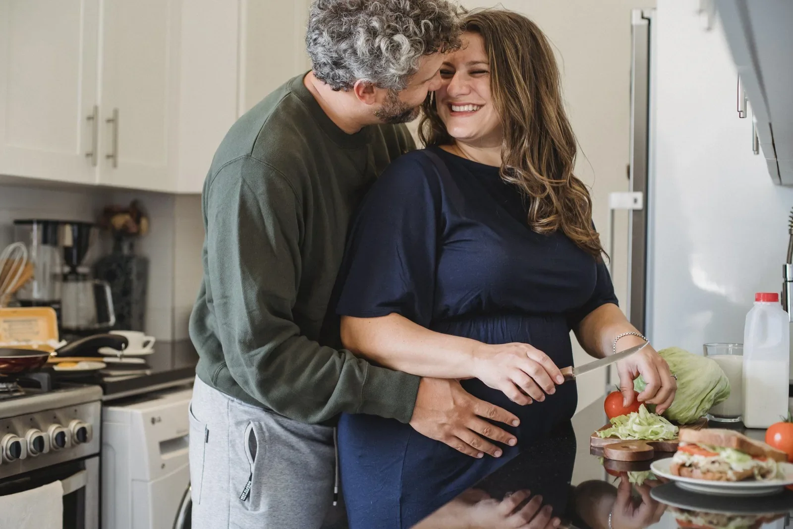 A couple laughing together while cooking side by side in a small kitchen
