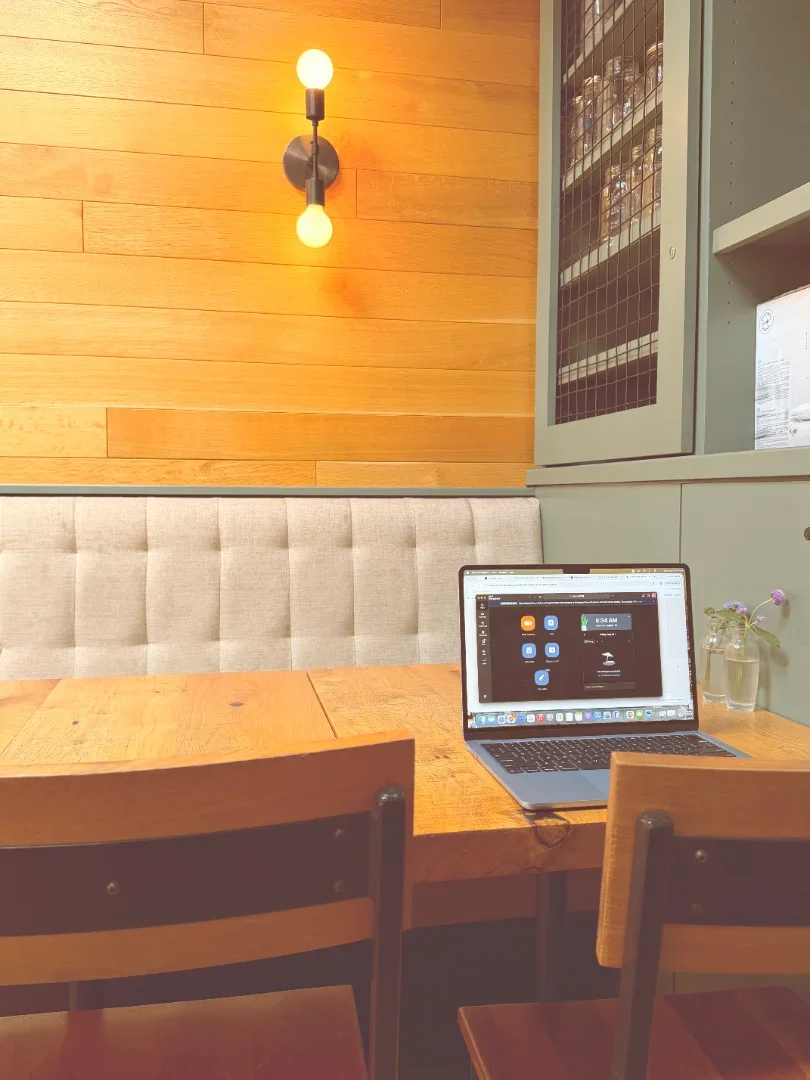 An open laptop on a wooden table in a quiet coffee shop, warm light on the wall behind