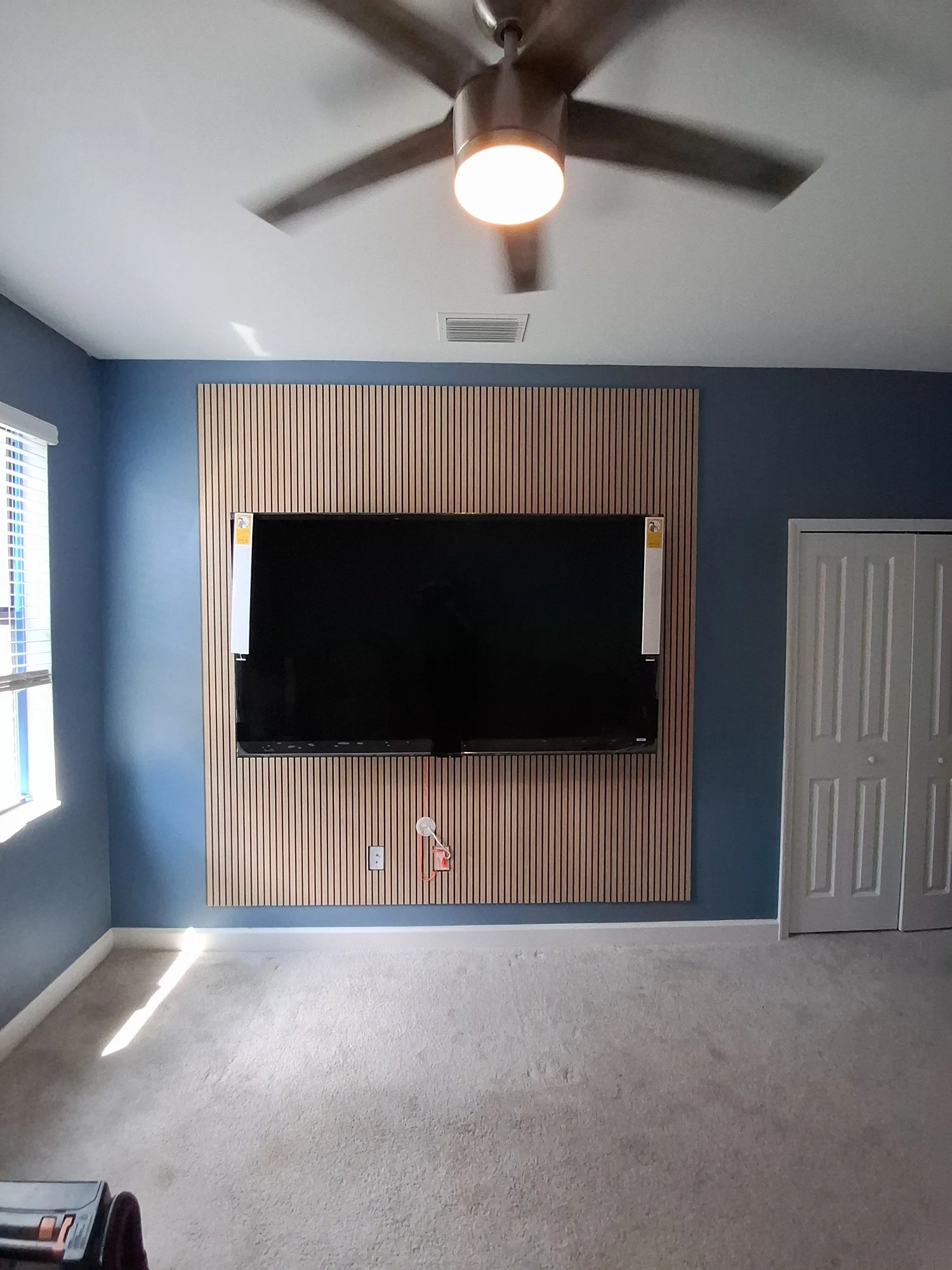 TV mounted on an accent wall with a new ceiling fan