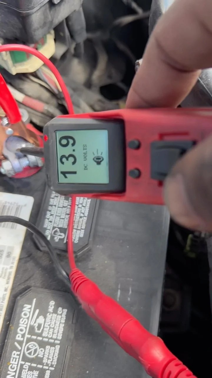 Technician testing a car battery with a probe reading 13.9 volts