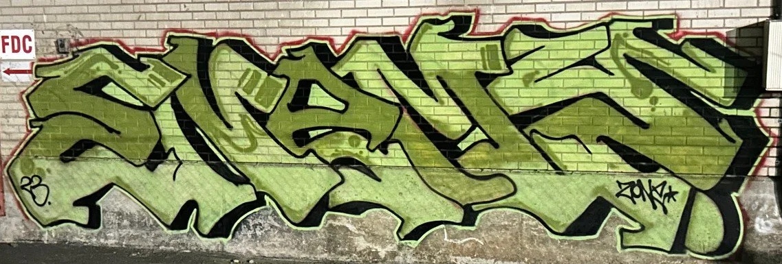 A wide green and silver style-writing piece on a brick wall.