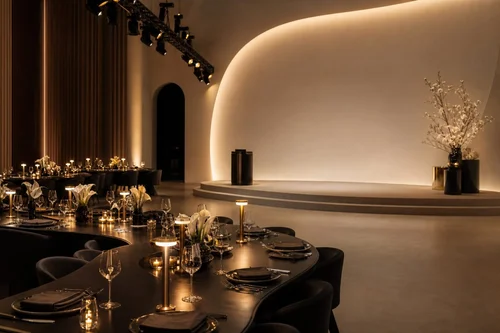 Refined corporate dinner in a warm-lit hall with dark tables and a curved illuminated stage.