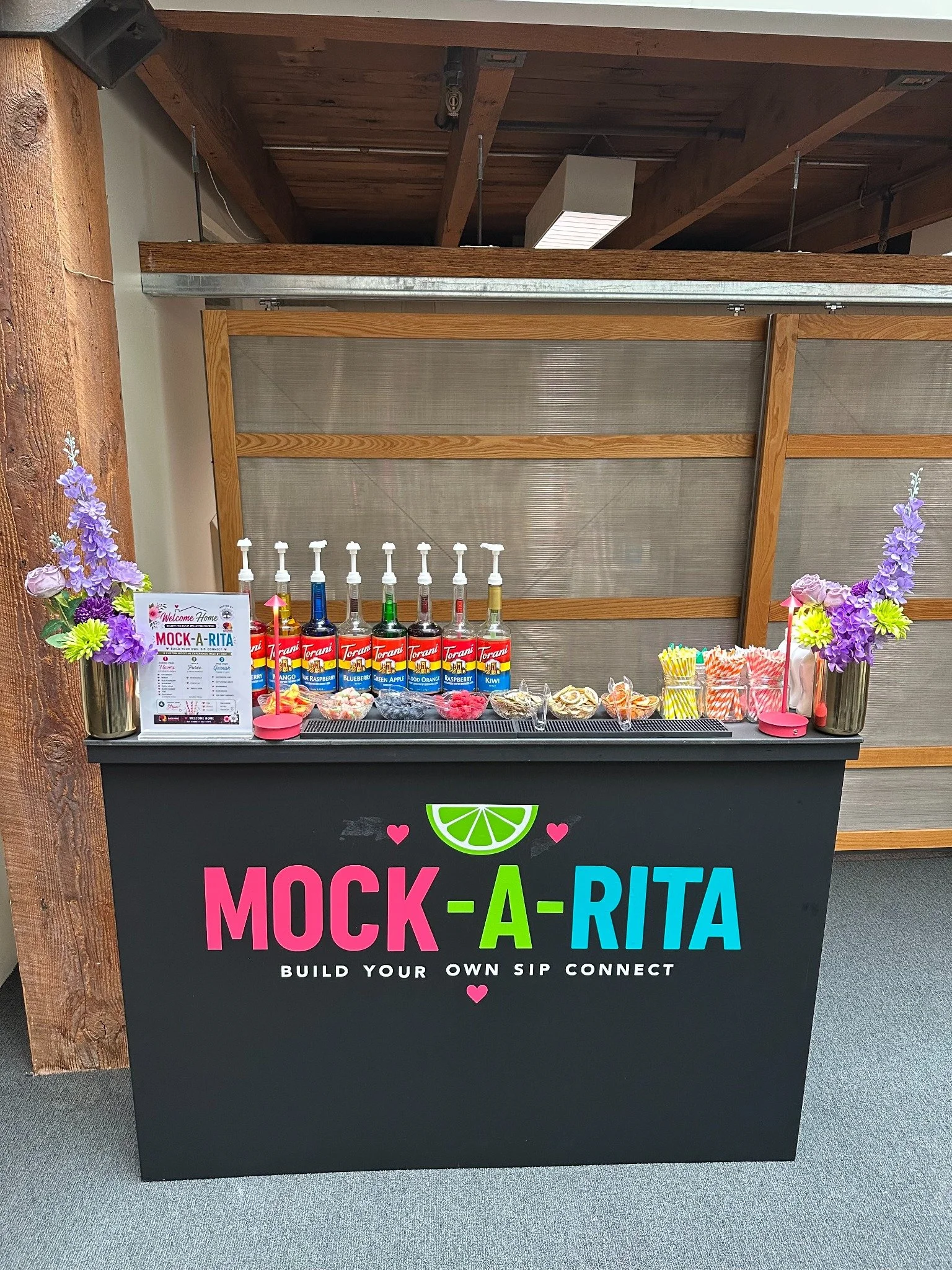 Mock-A-Rita bar with colorful syrups, garnishes, striped straws, and purple floral arrangements