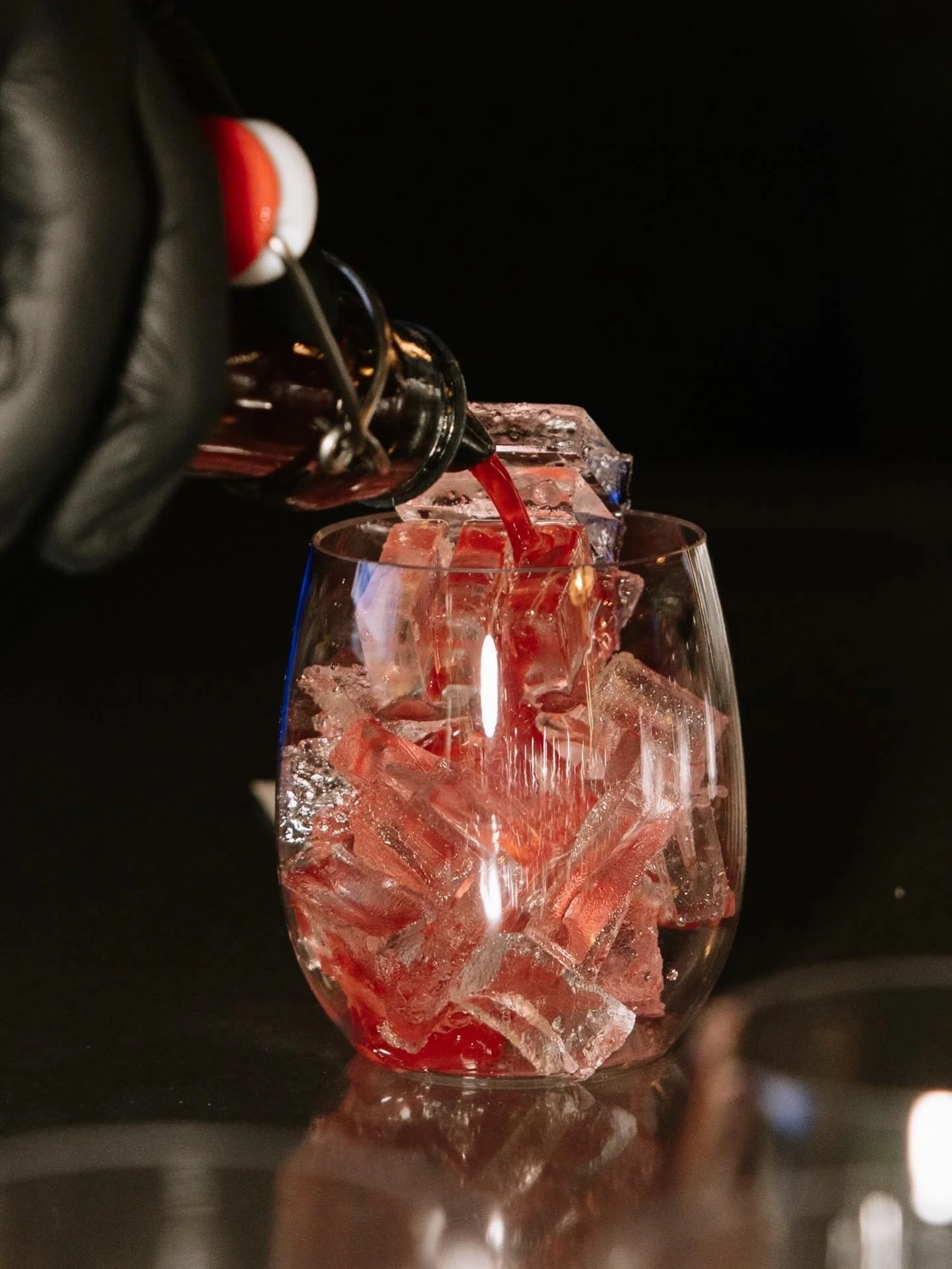 Black-gloved bartender pouring a red cocktail