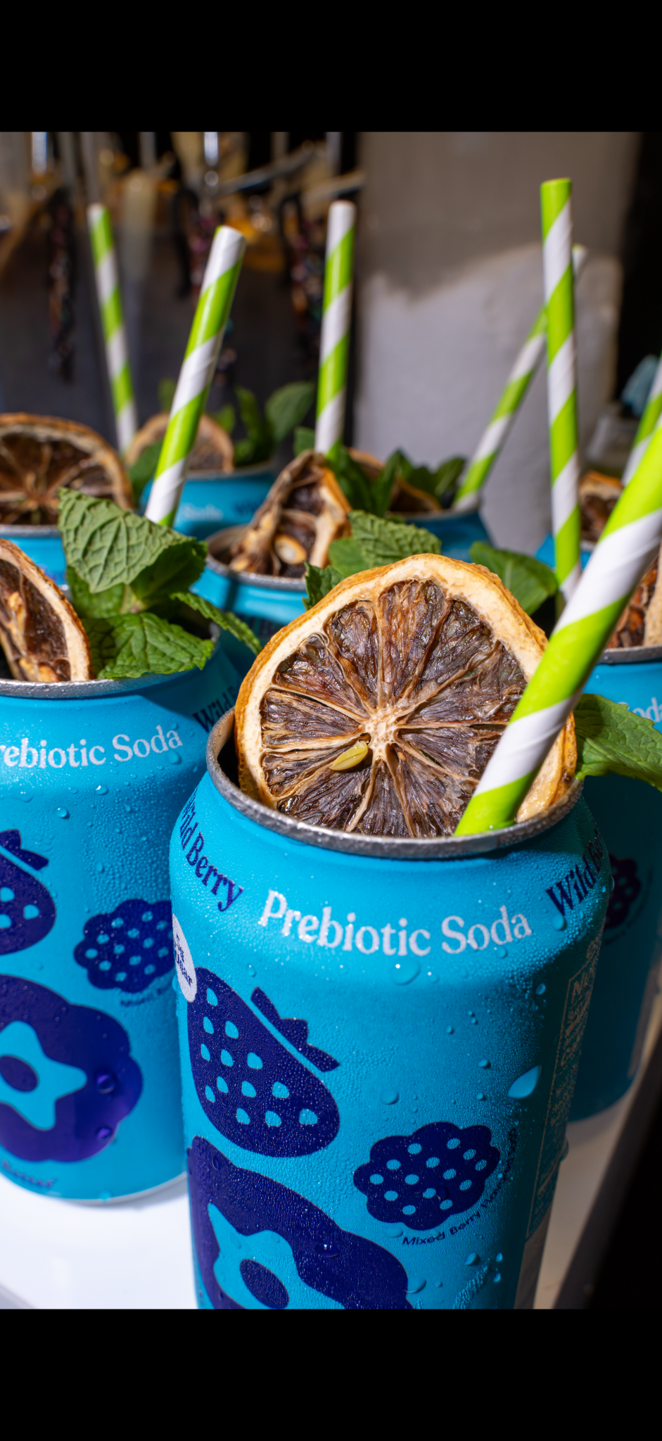 Blue blackberry prebiotic soda cans garnished with dried citrus, mint, and striped straws