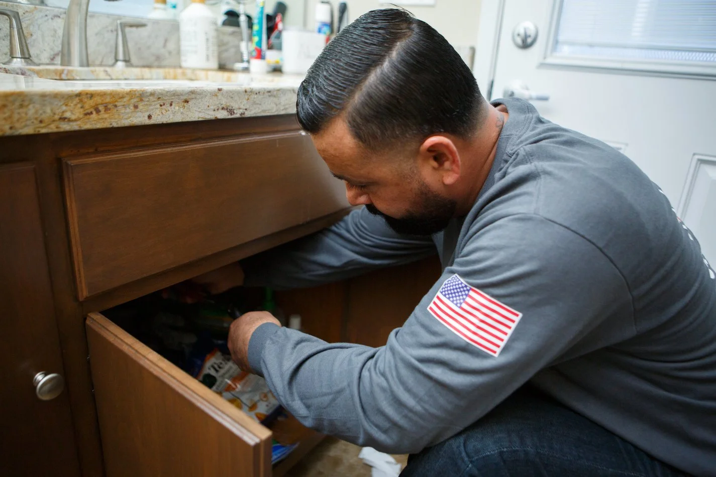 Ser Plumbing plumber checking a fixture supply inside a base cabinet