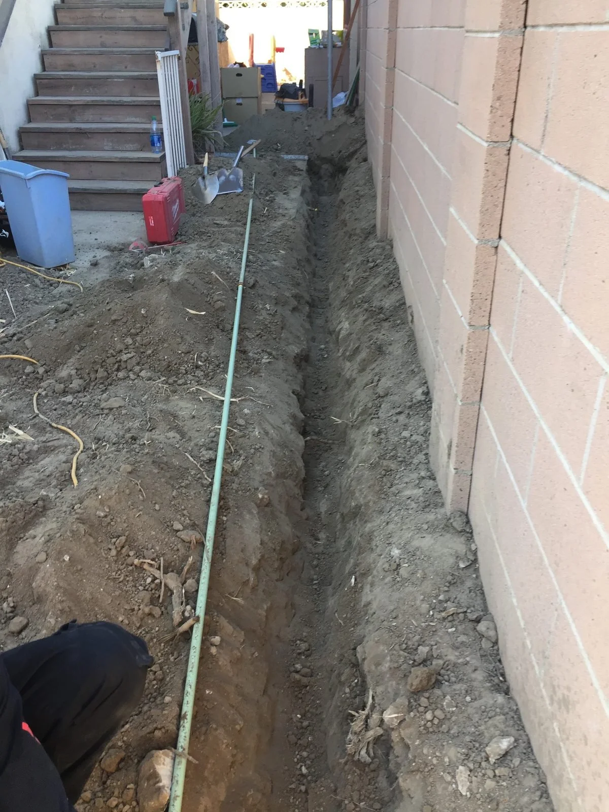 Open trench dug alongside a block wall for a new underground line — Ser Plumbing, Southeast LA County