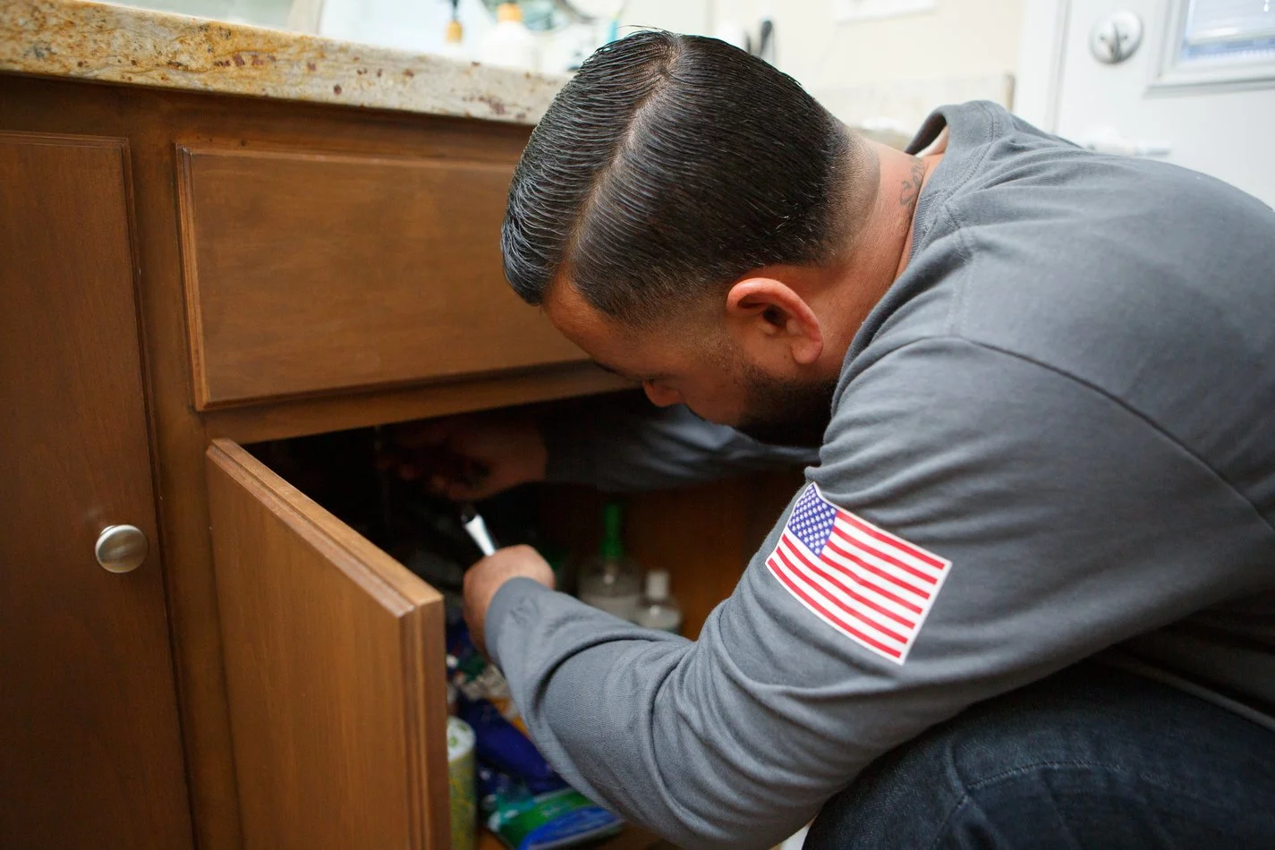 Ser Plumbing plumber reaching into an under-sink cabinet during a repair