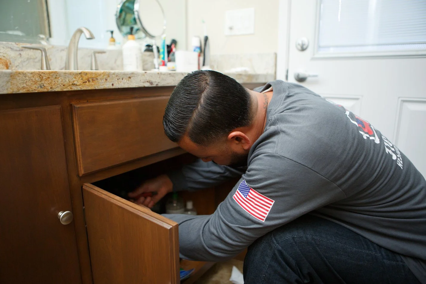 Ser Plumbing technician kneeling at an open cabinet under a sink