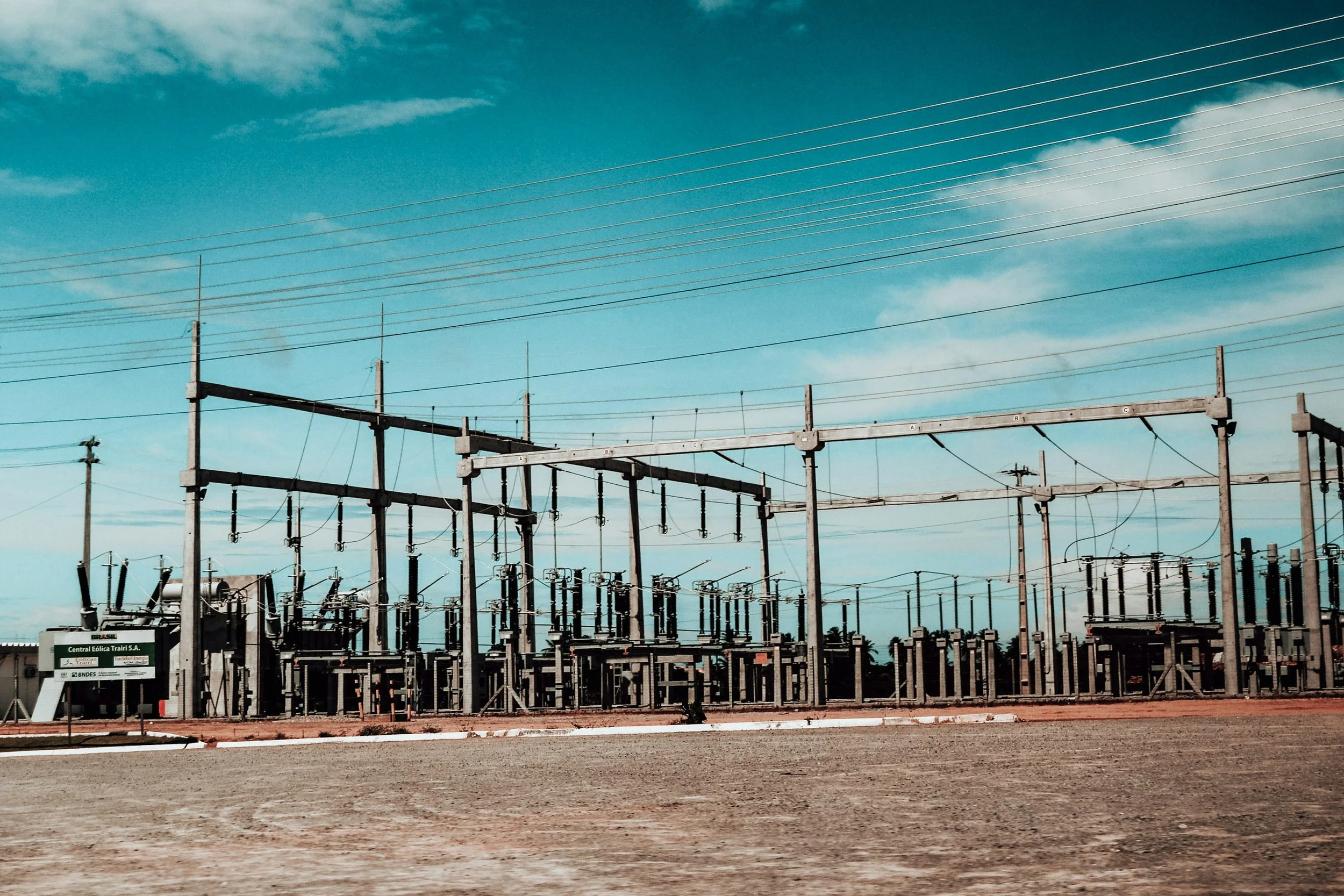 Electrical substation with steel gantries, insulators and overhead power lines beneath a cloudy blue sky
