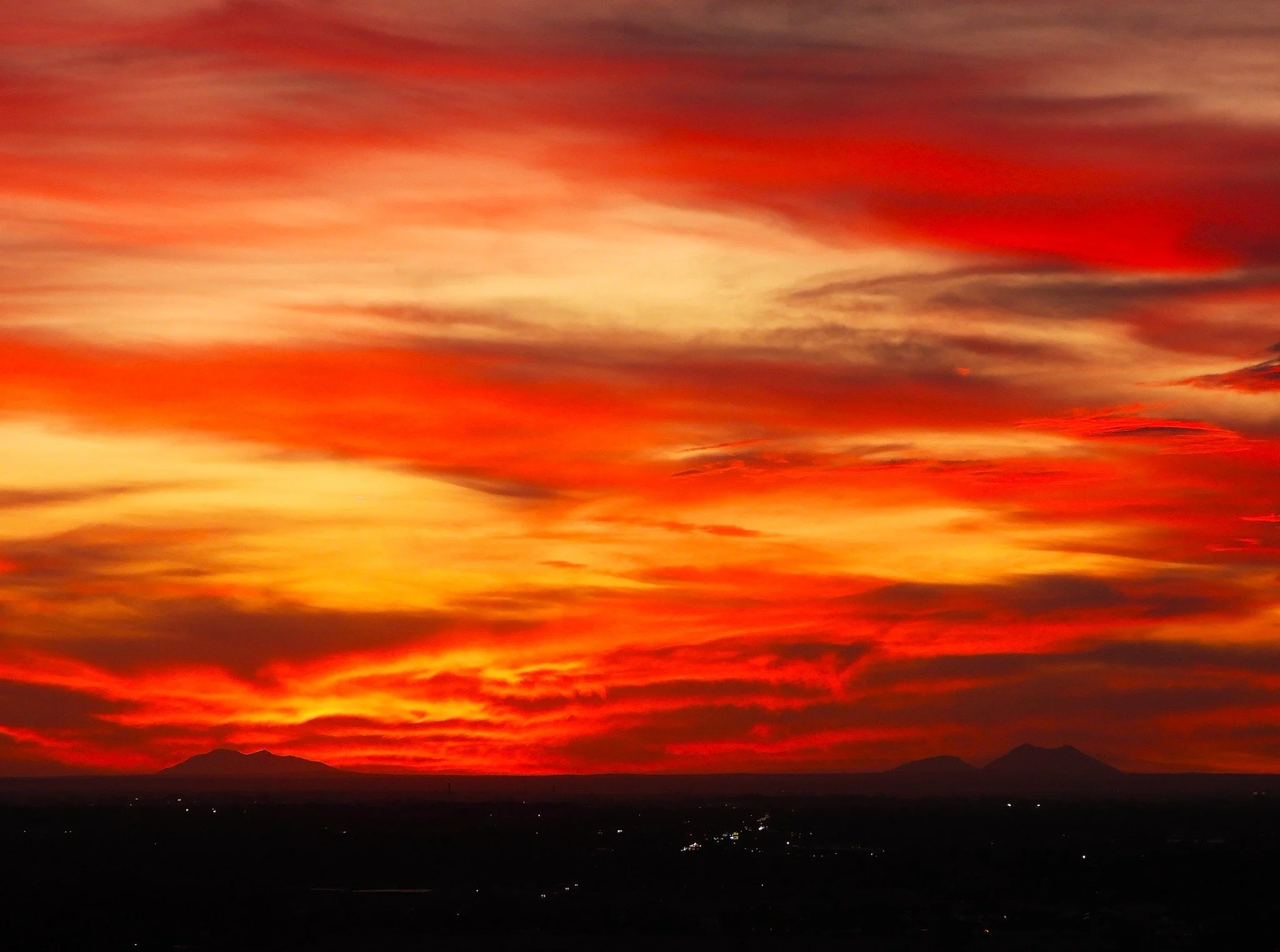 Red and gold clouds fill the sky above dark mountain silhouettes and distant lights.