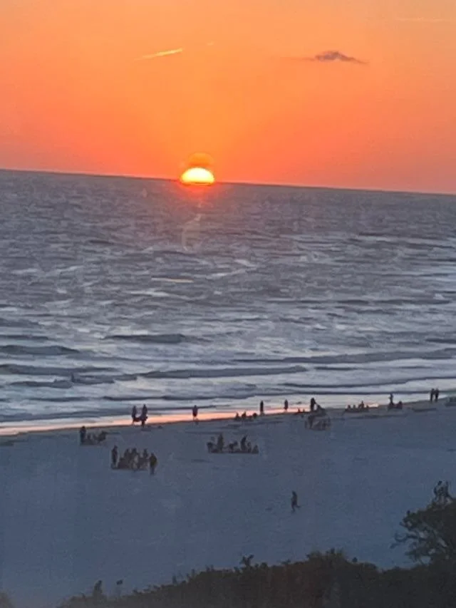 Silhouettes of people walking along the beach at sunset with the sun low over the water