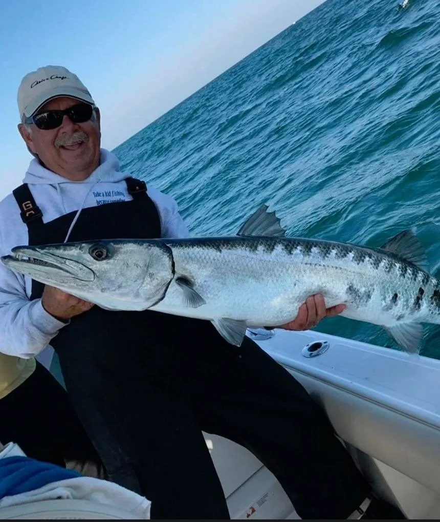 An angler on a fishing boat smiling and holding up a large barracuda he caught