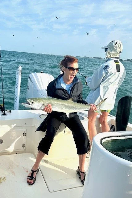 A woman on a fishing boat holding up a large fish with an excited expression