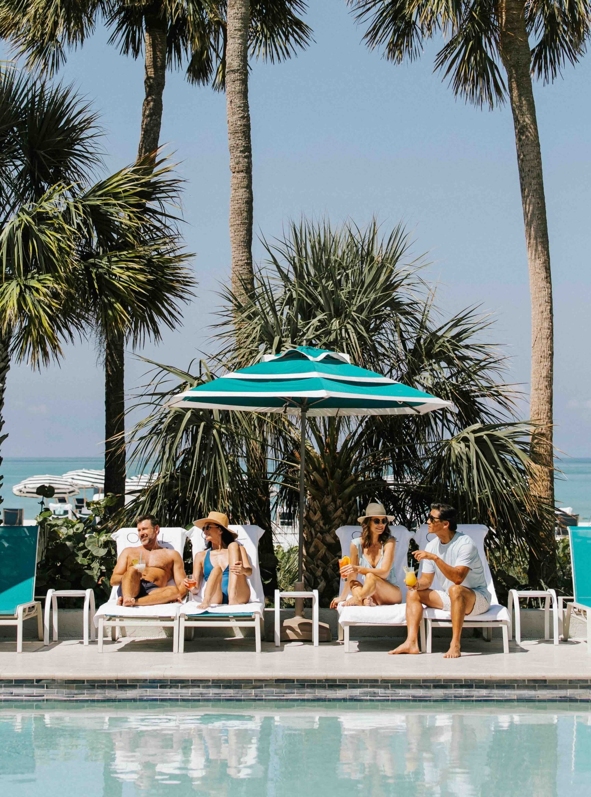 Guests relaxing by the resort pool under palm trees and cabanas at The Resort at Longboat Key Club