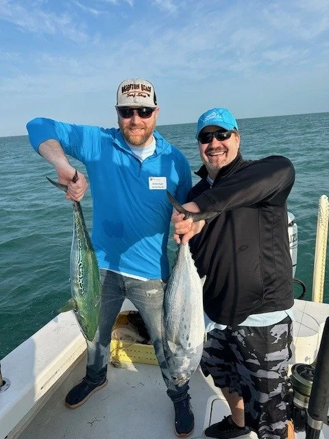 Two men on a fishing boat each holding up a fish they caught