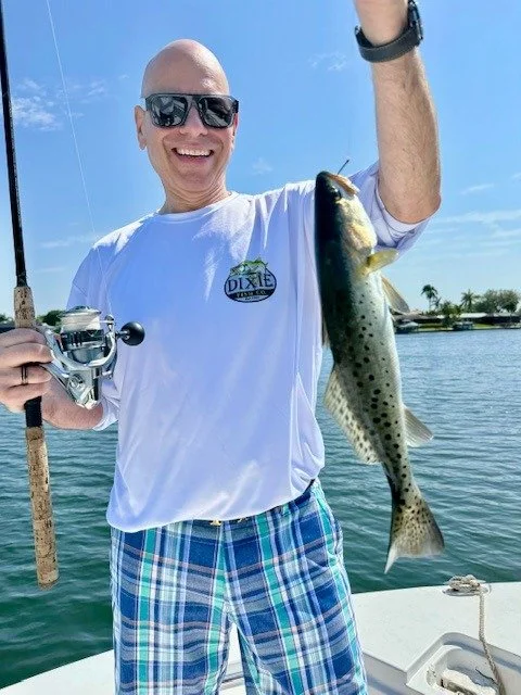 A man on a fishing boat smiling and holding up a spotted seatrout he caught