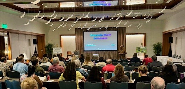Attendees seated in a conference room watching a presentation slide titled Computer World Domination