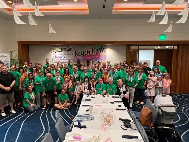 A large group of attendees in matching green Beach Bash BBQ t-shirts posing together in a banquet room
