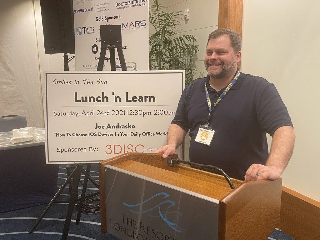 A presenter smiling behind a podium next to a sign for a Smiles in the Sun Lunch 'n Learn session
